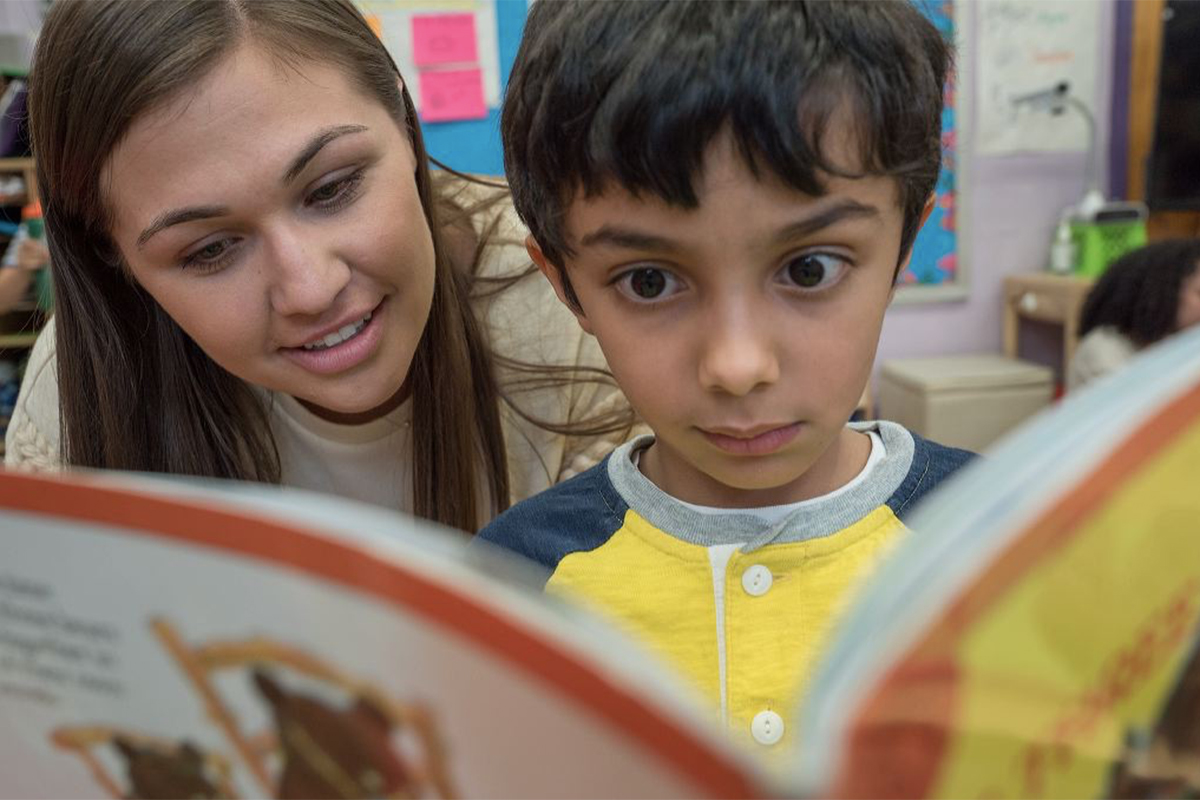 A teacher works with a child on reading a book.