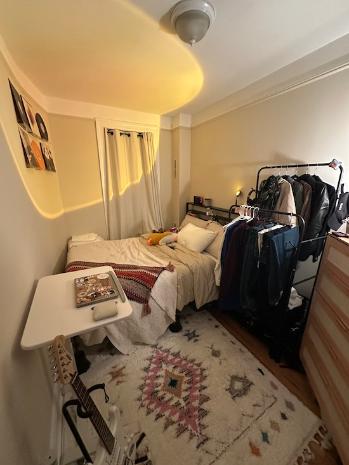 A bedroom in NYC with a bed against the back wall, a desk, and a dresser against the other walls.