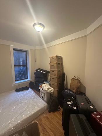 A room in an NYC apartment with a mattress and moving boxes in one corner.