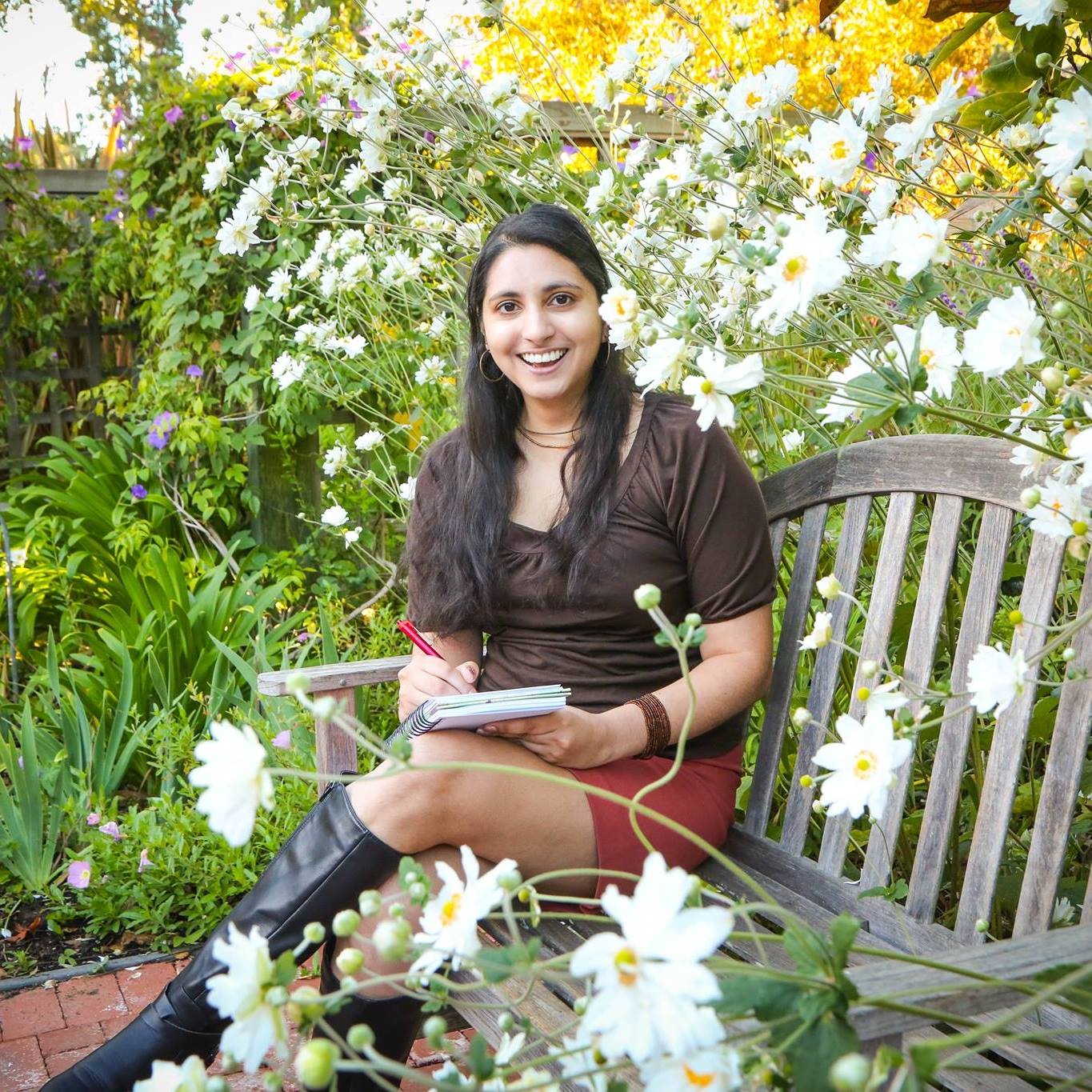 Photo of Pavita sitting on a wooden bench outdoors surrounded by blooming white flowers.