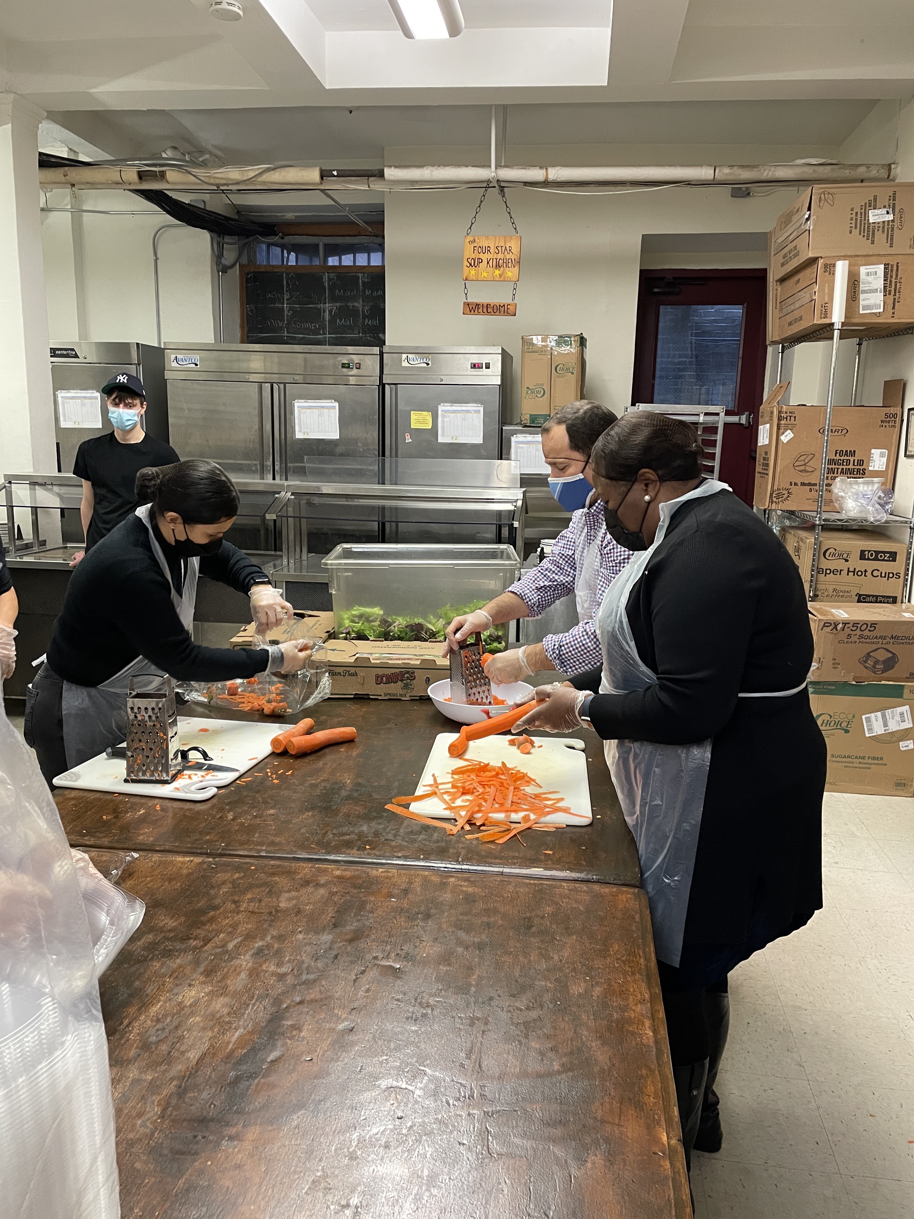 Folks preparing food on a table with cutting boards and wearing aprons and hair nets. 