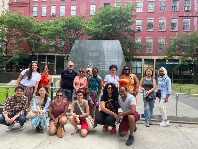 Group of folks gathered for a photo outdoors by a monument. 