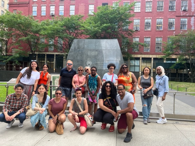 Group of folks gathered for a photo outdoors by a monument. 