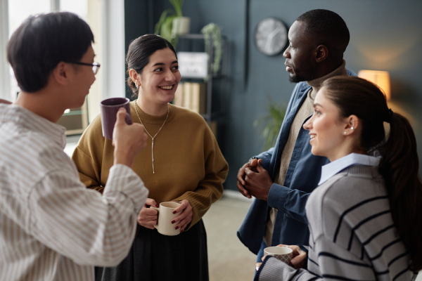 Group of four cheerful adults chatting and enjoying coffee break