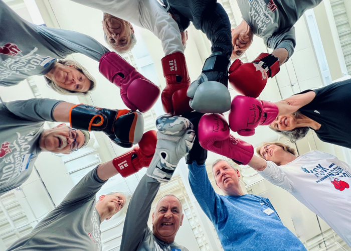 Group with boxing gloves huddled in circle with one arm in center