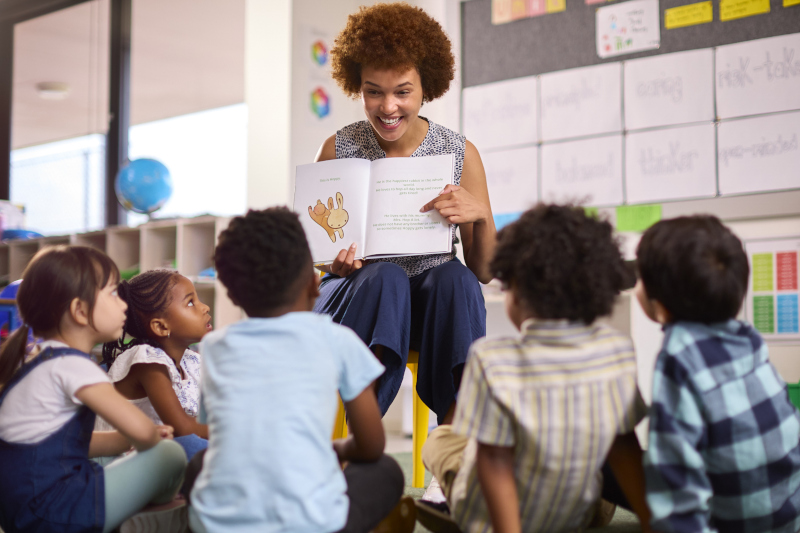 A teacher holding up an open book to show the pages to her students