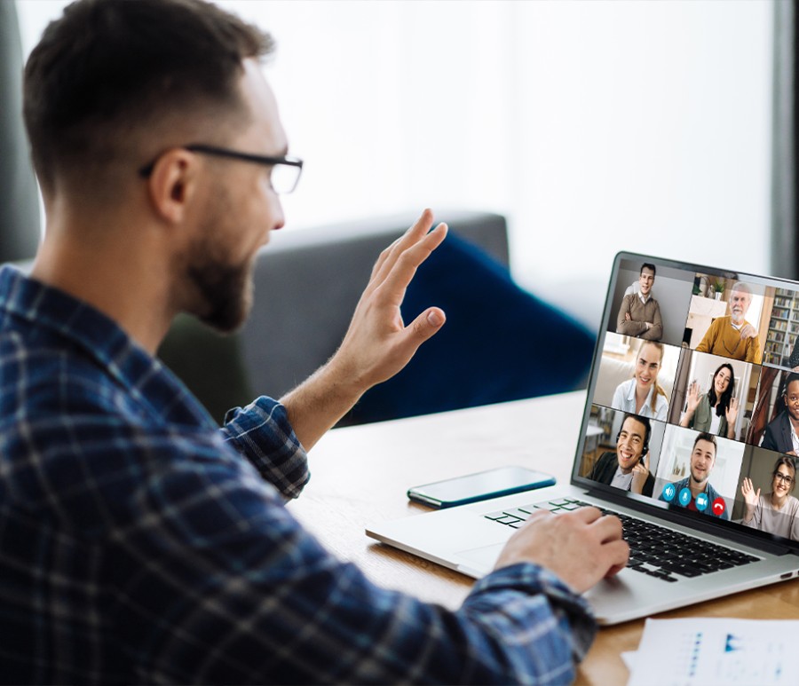 A professor on a laptop waving to students taking an online course