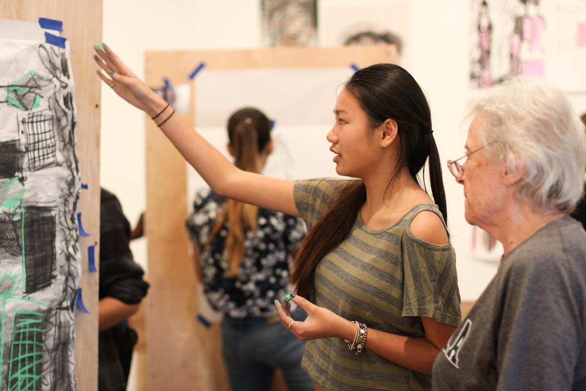 Two people standing in front of a piece of art. One is gesturing to the art with one hand.