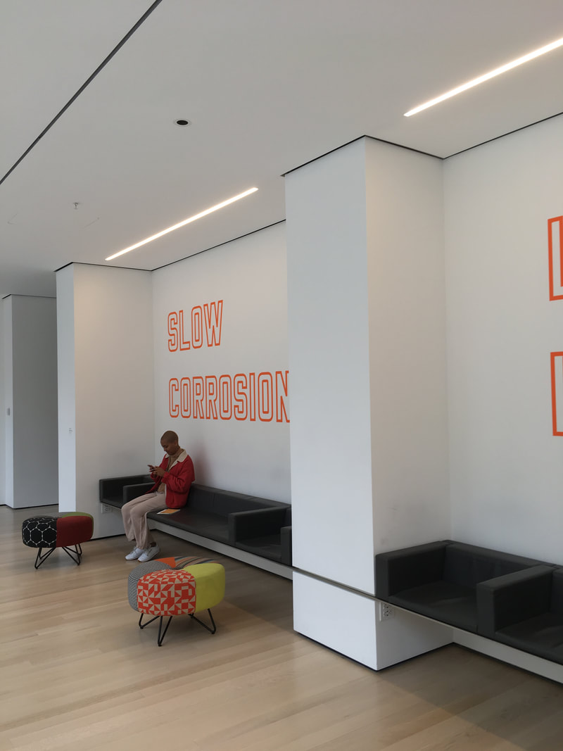 Person sitting against white wall with neon orange lettering on it