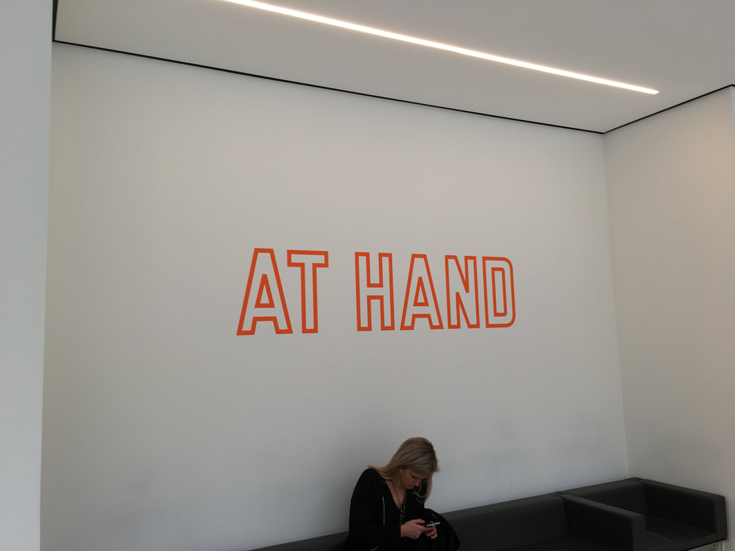Neon orange lettering that says At Hand set against a white wall