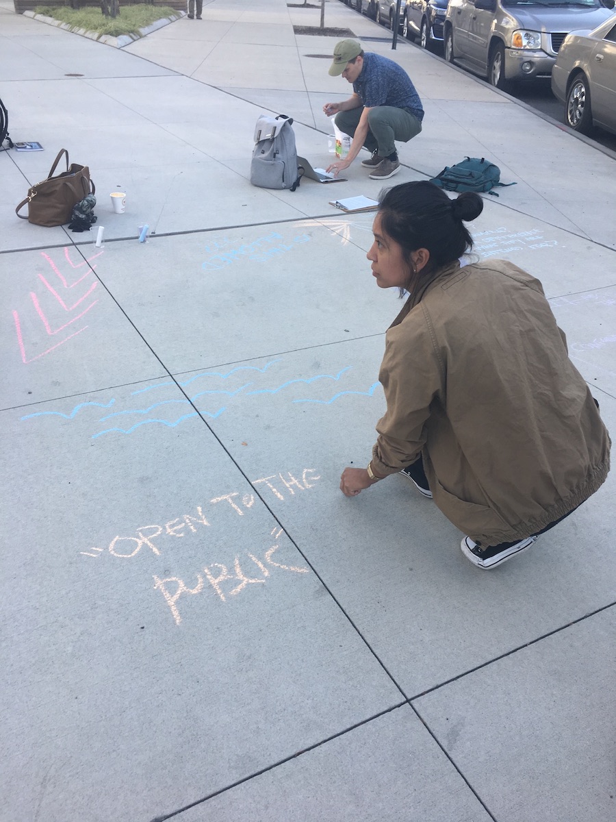 person kneeling on the side walk with chalk in their hand next to open to the 