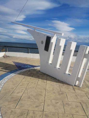 A white sculpture in the form of a boat prow faces the water.
