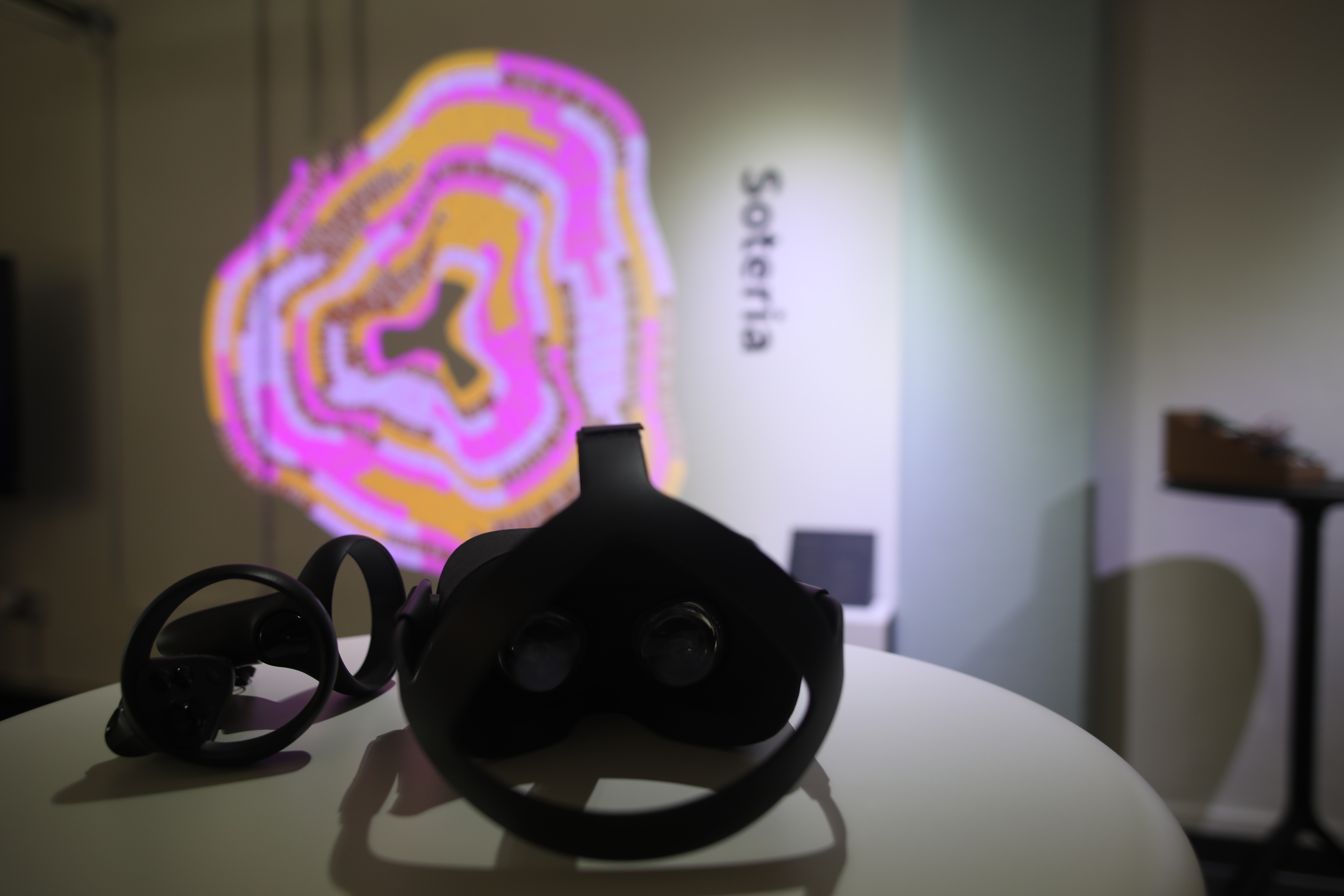Oculus goggles on white table in front of the squiggly image with the word soteria repeated 