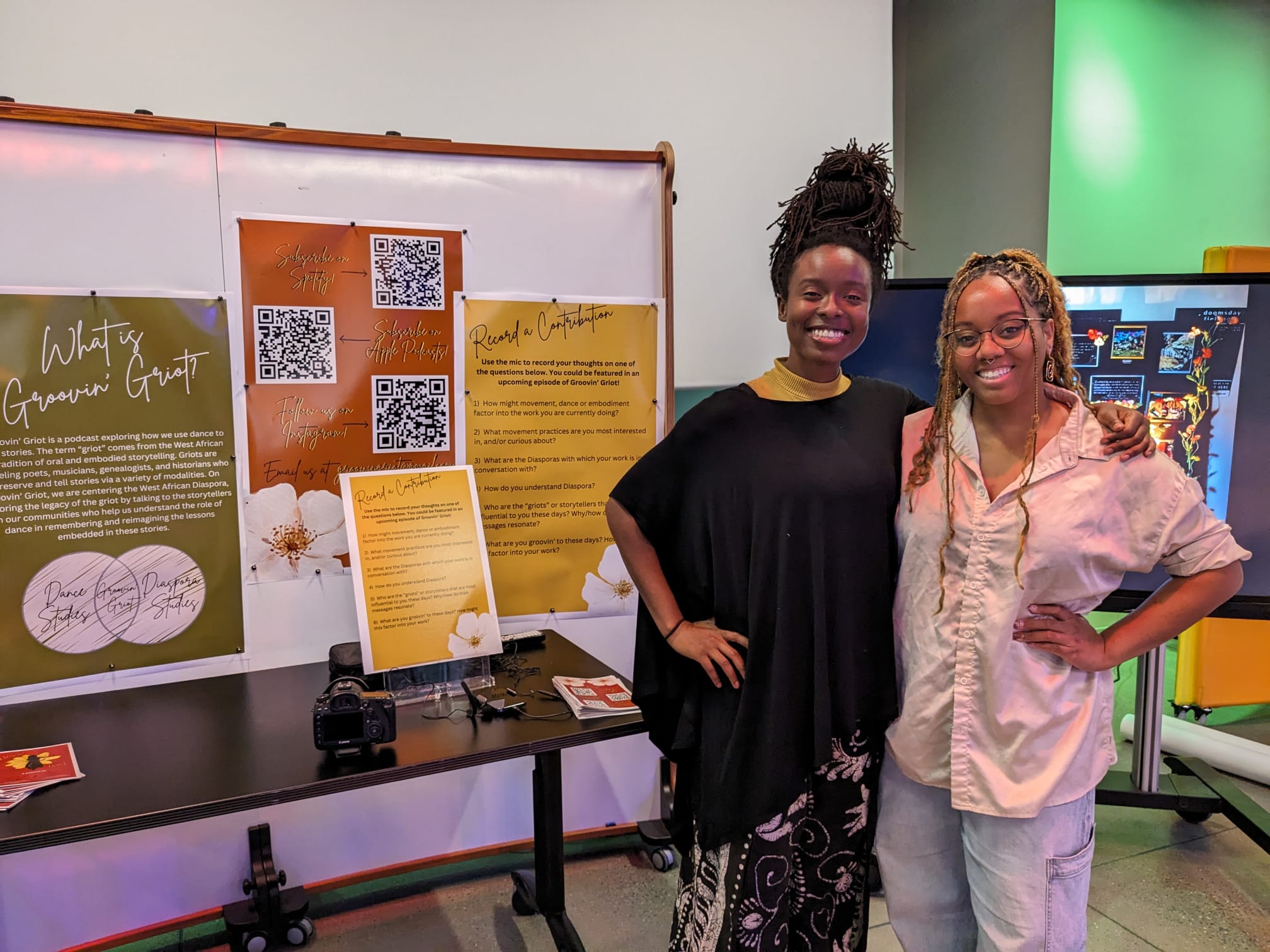 Groovin Griot Hosts Ore and Azsaneé standing in front of a whiteboard with posters about the podcast