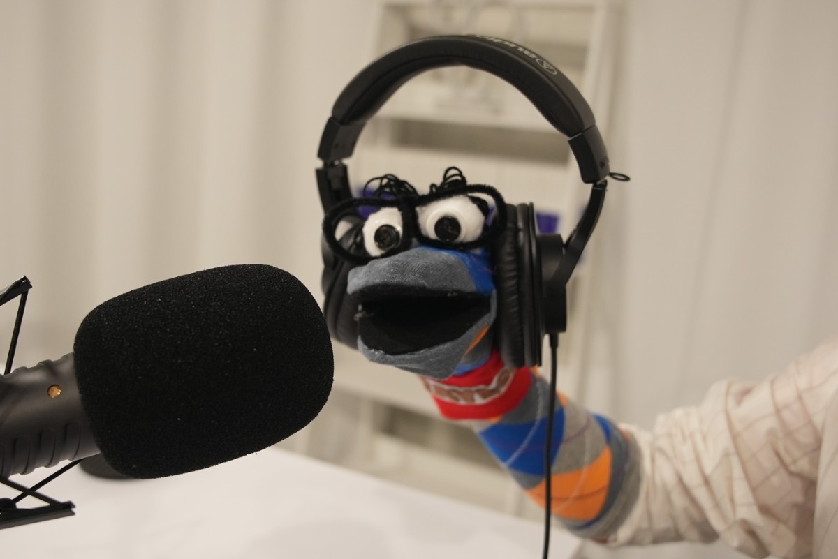 a sock puppet wearing headphones at a microphone in a studio