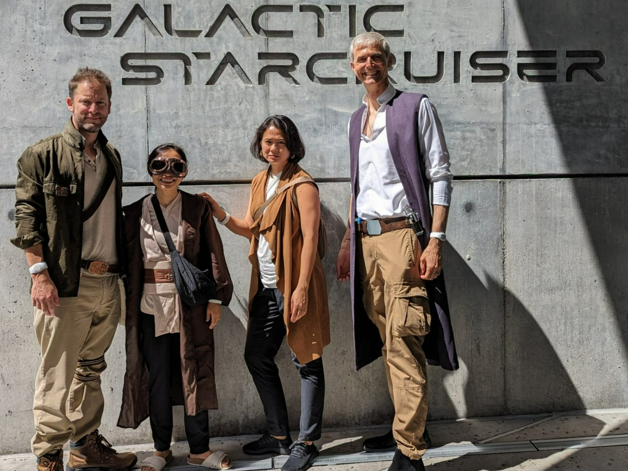 four costumed adults standing in front of cement wall with lettering on it