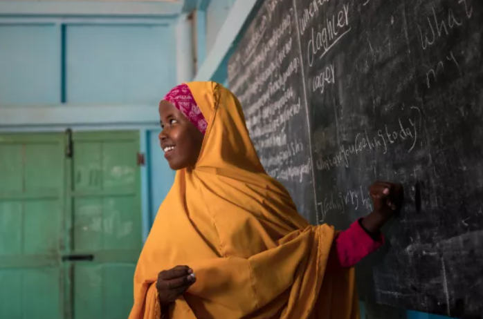 African woman gesturing towards chalkboard