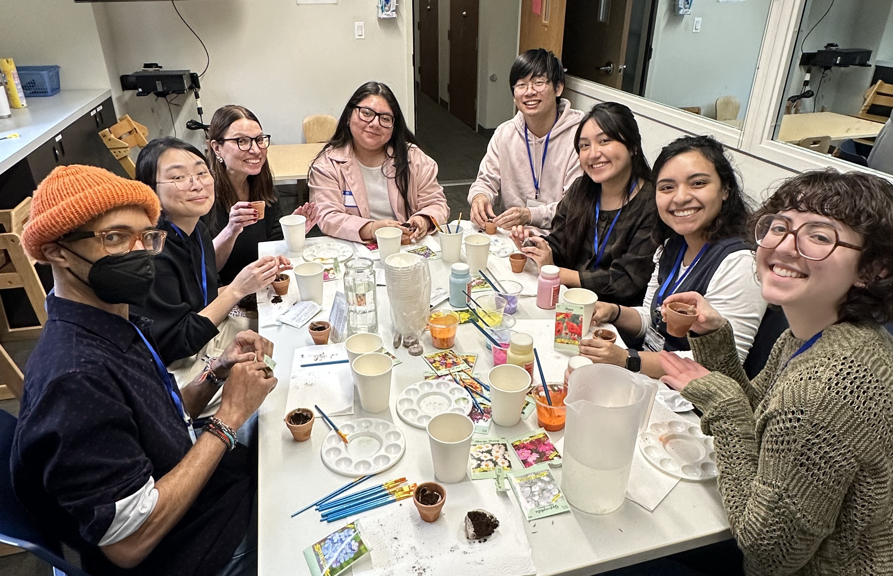 Clinicians and participants in the Saturday Aphasia Group seated around a table painting small pots and planting flower seeds during a gardening activity