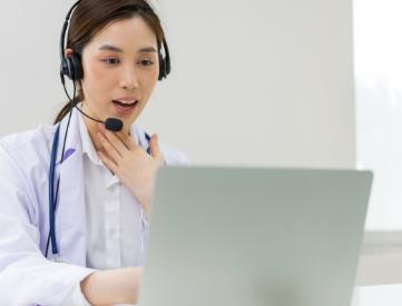 Speech-language clinician conducting a virtual therapy session on a laptop while wearing a headset