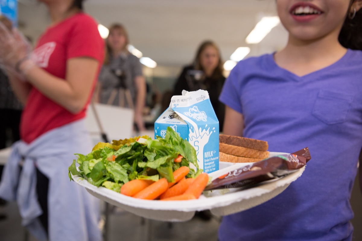 A kid holding a bountiful plate of lunch 