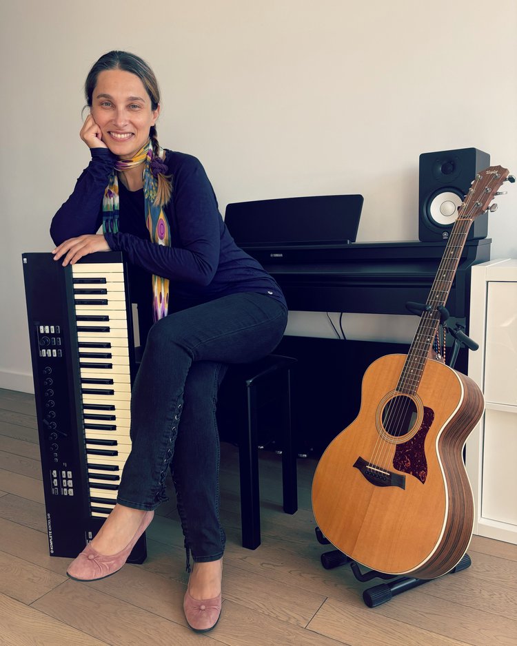 A woman, seated at a piano next to an acoustic guitar, leaning on an upright electronic keyboard