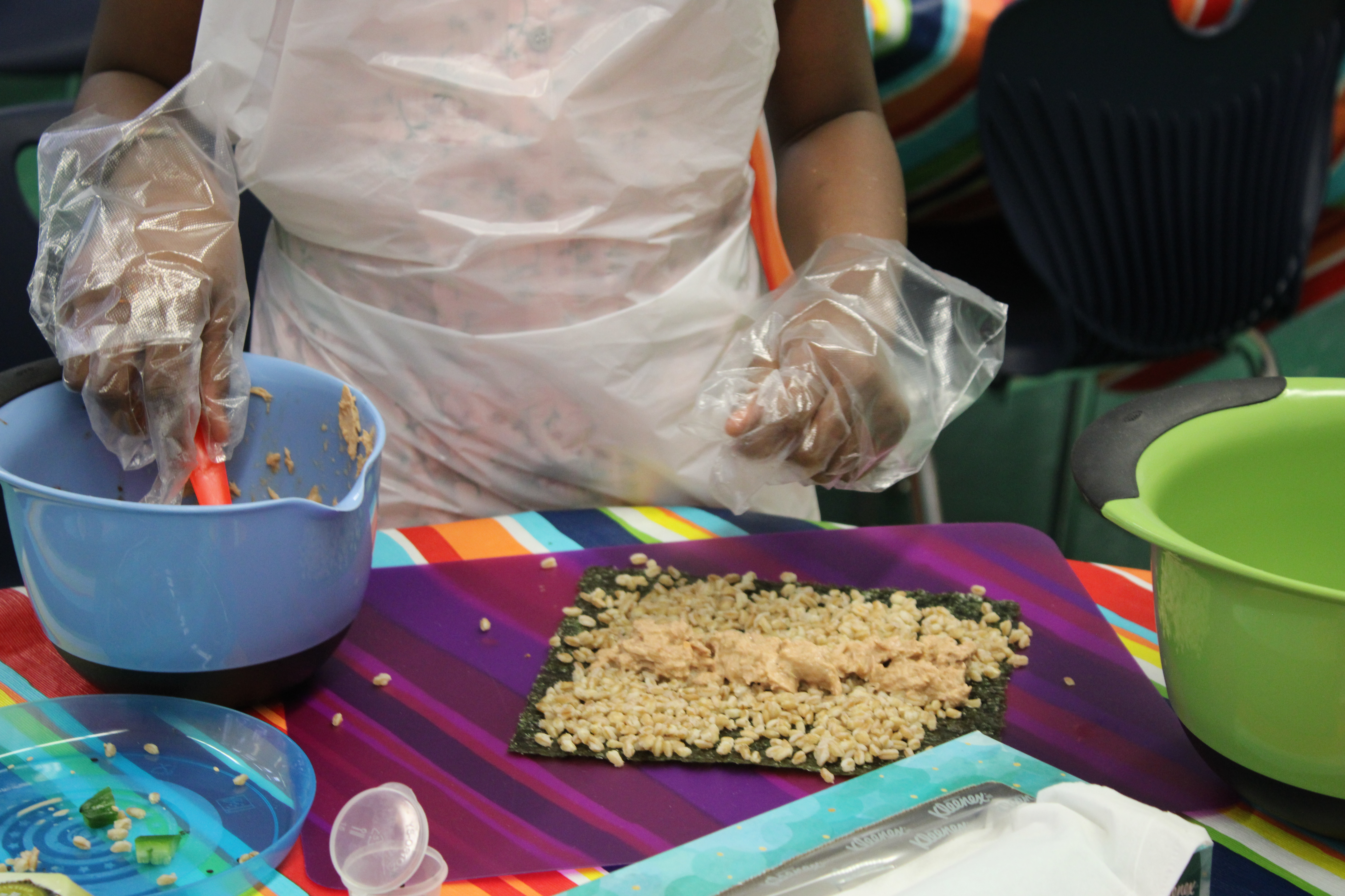 a young person in an apron and plastic gloves makes sushi