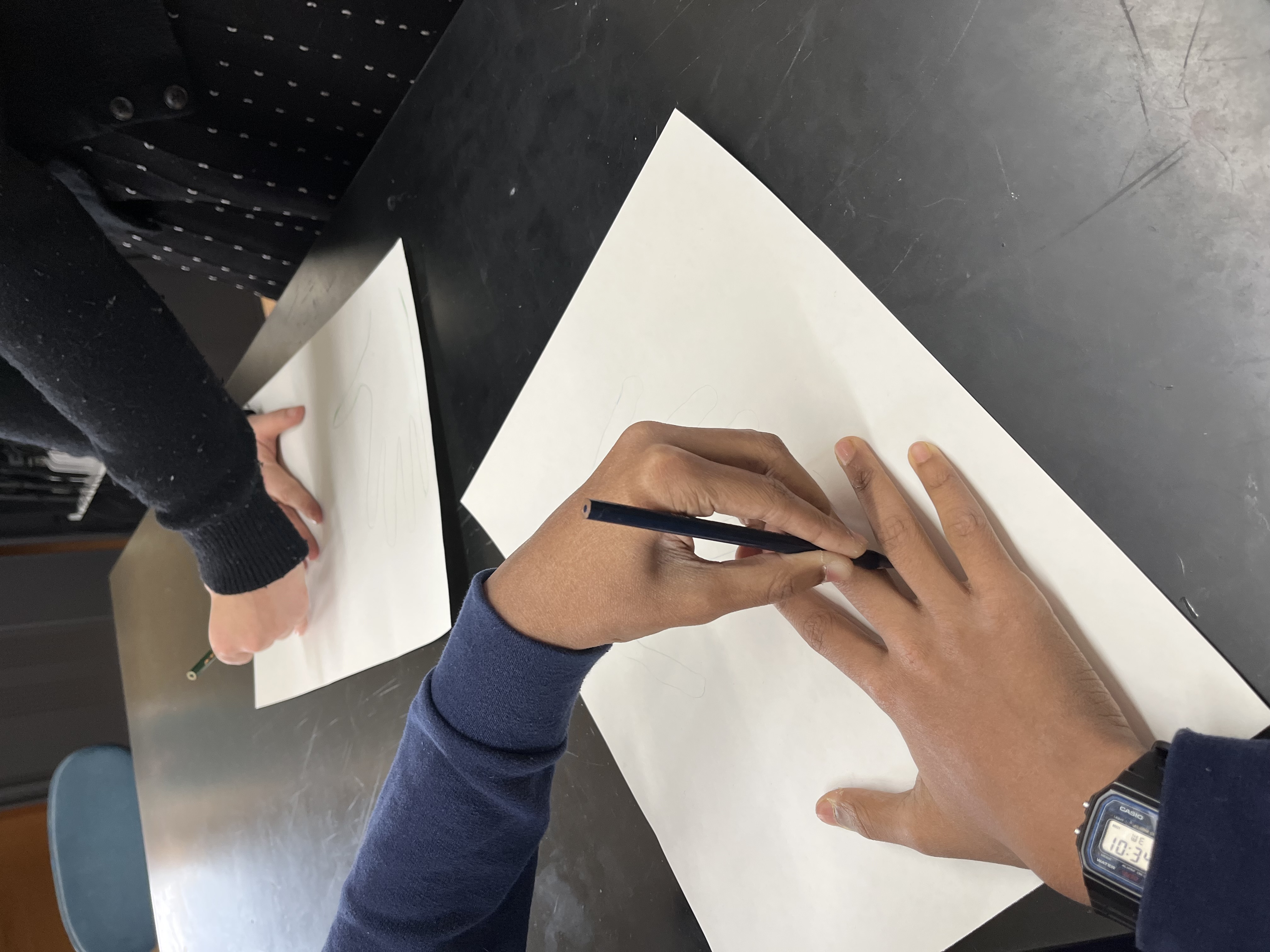 Two young people trace an outline of their hands on a piece of paper using a pen