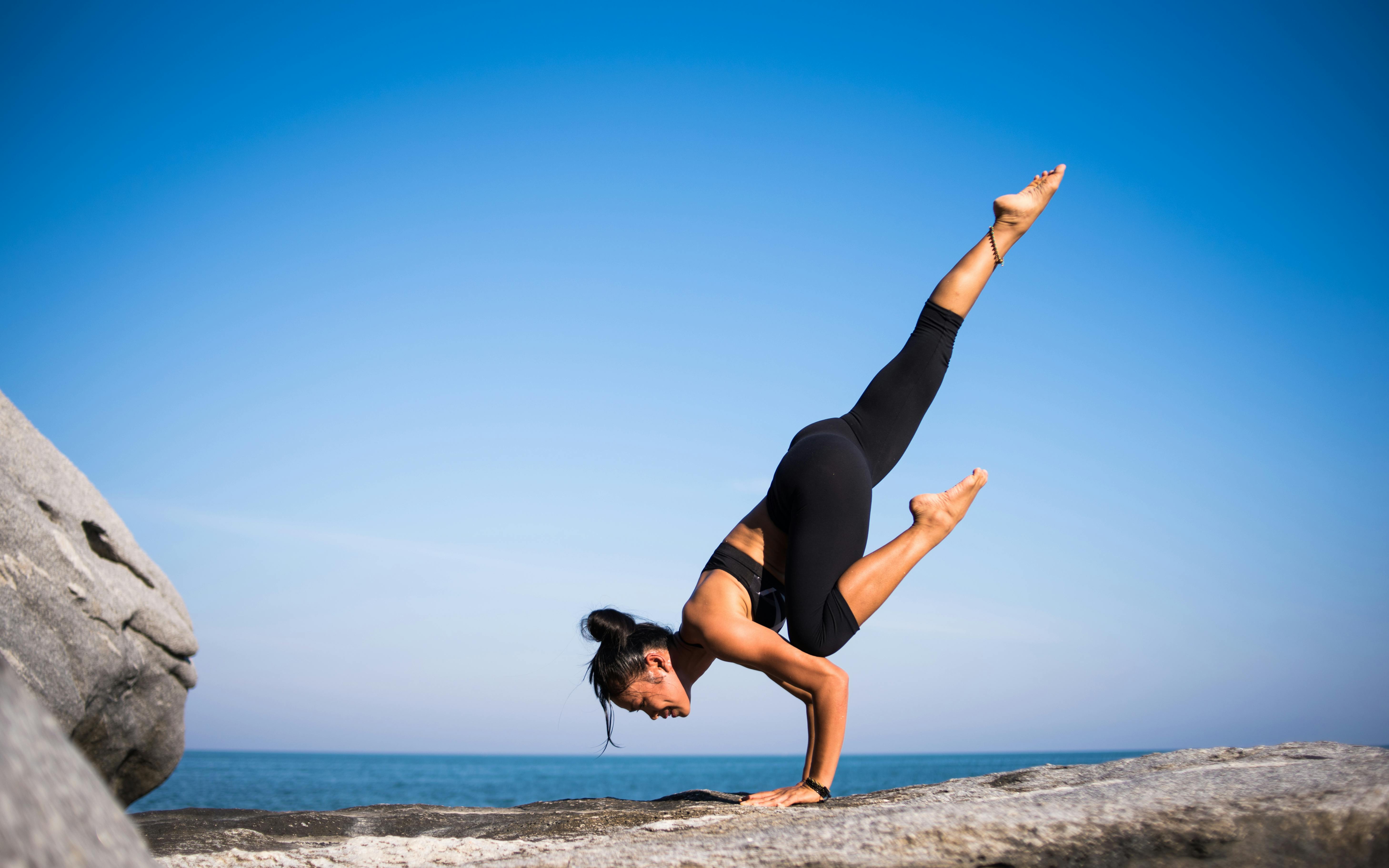 a young woman doing a partial handstand on top of a rock surface