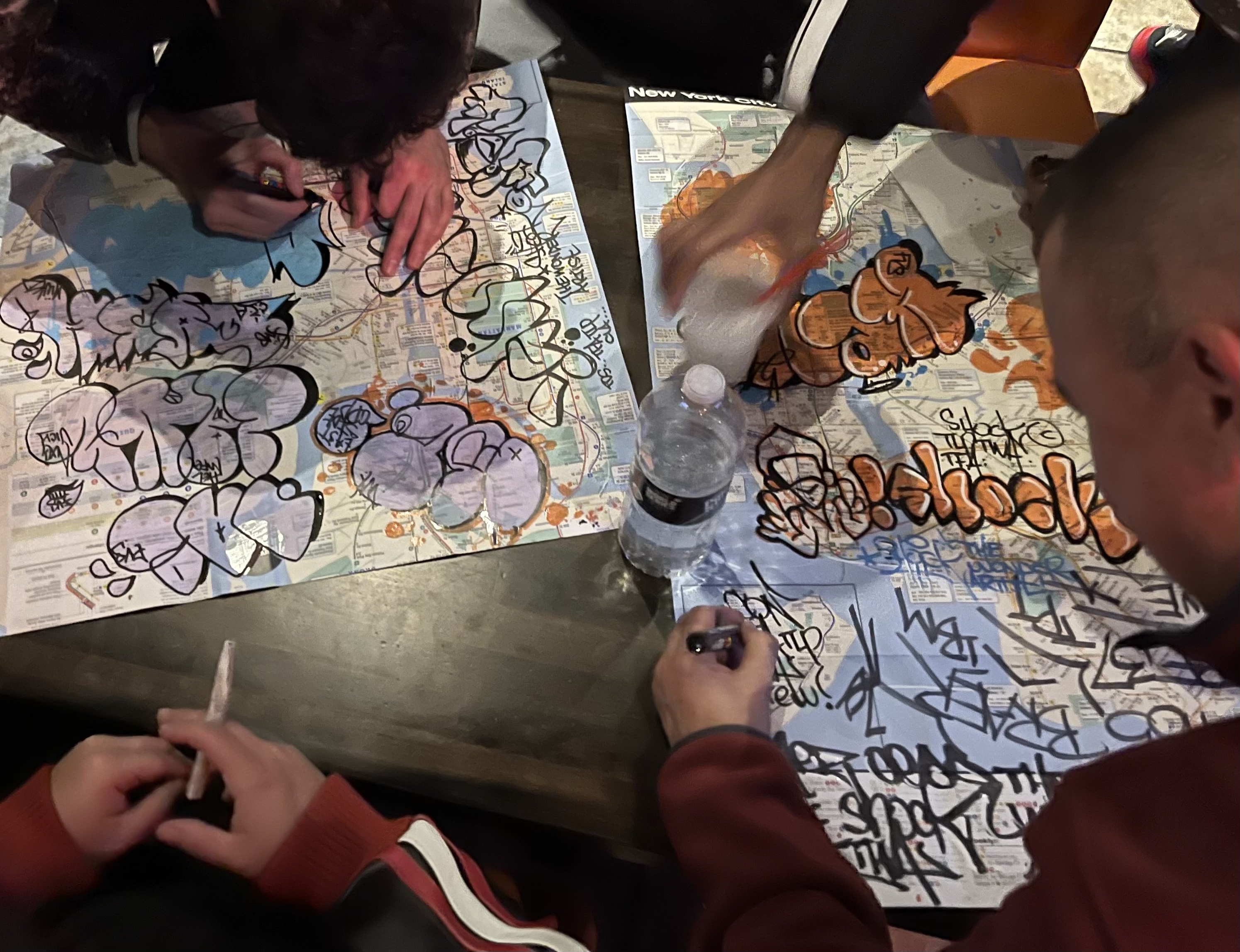 A image, taken from above, of multiple graffiti writers tagging on paper
