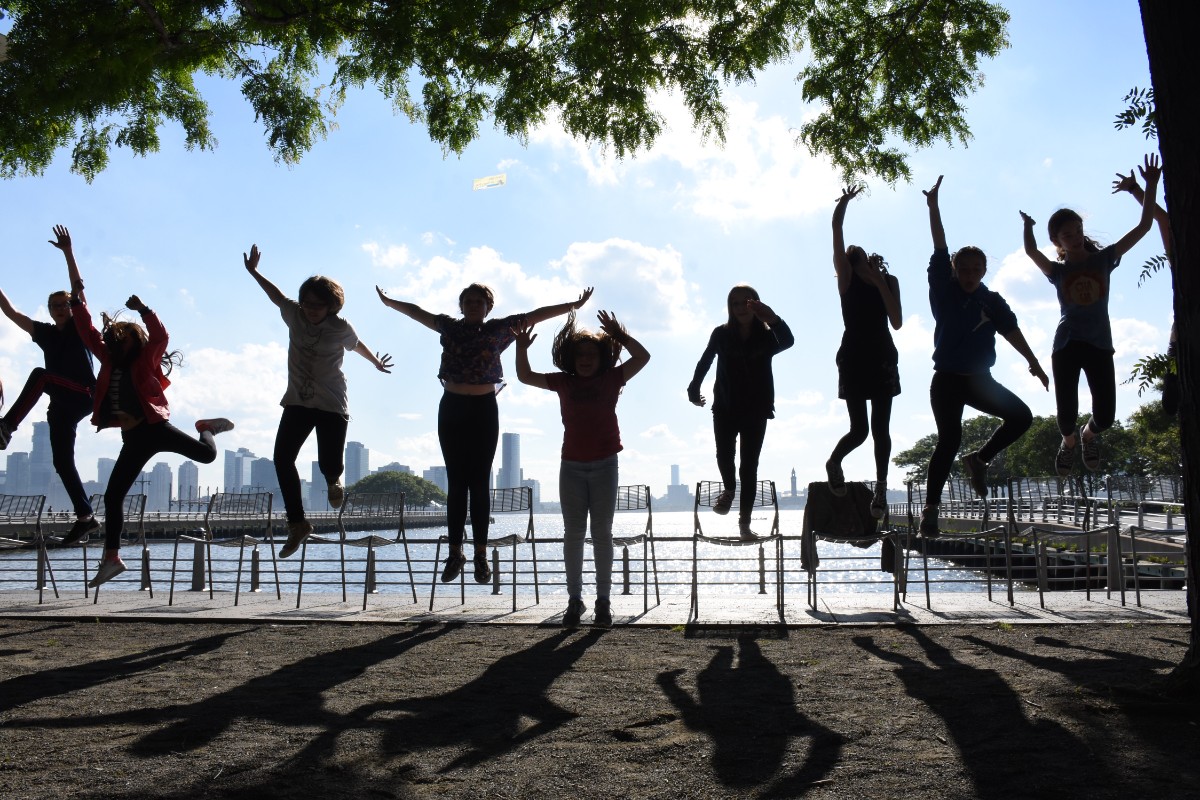 Students in a row in a mid-jump position with a river and city skyline in the background