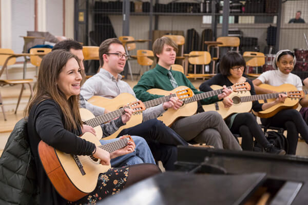 students holding guitars and sitting in a row in a music classroom