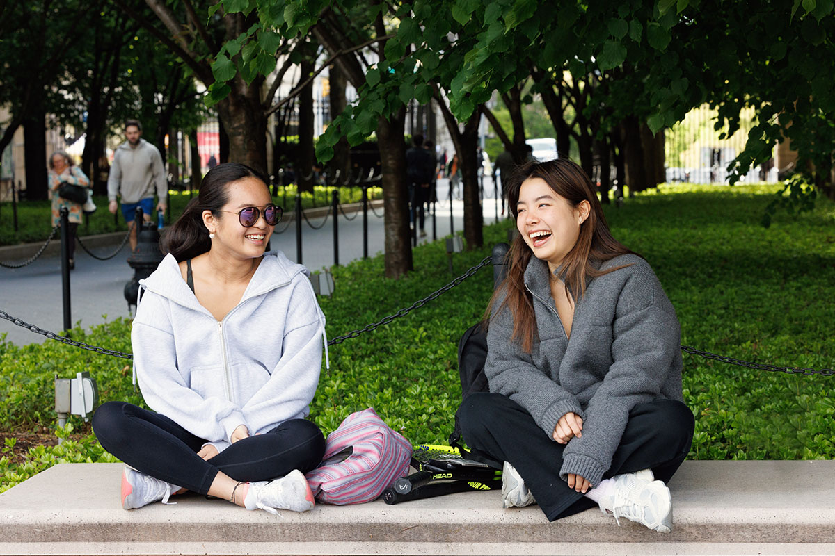 Students sitting on a bench on the Columbia University campus laughing and chatting