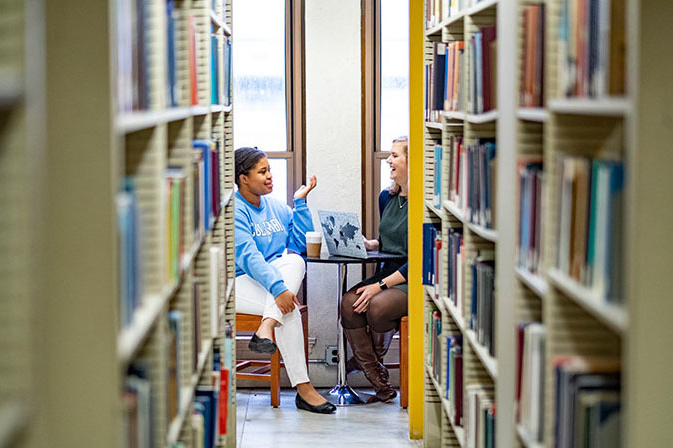 Two students having a discussion in the TC Library