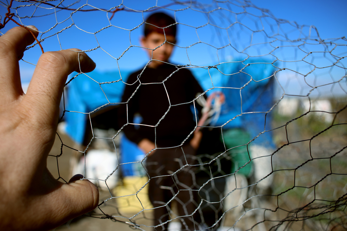A photo of a refugee behind a wire fence