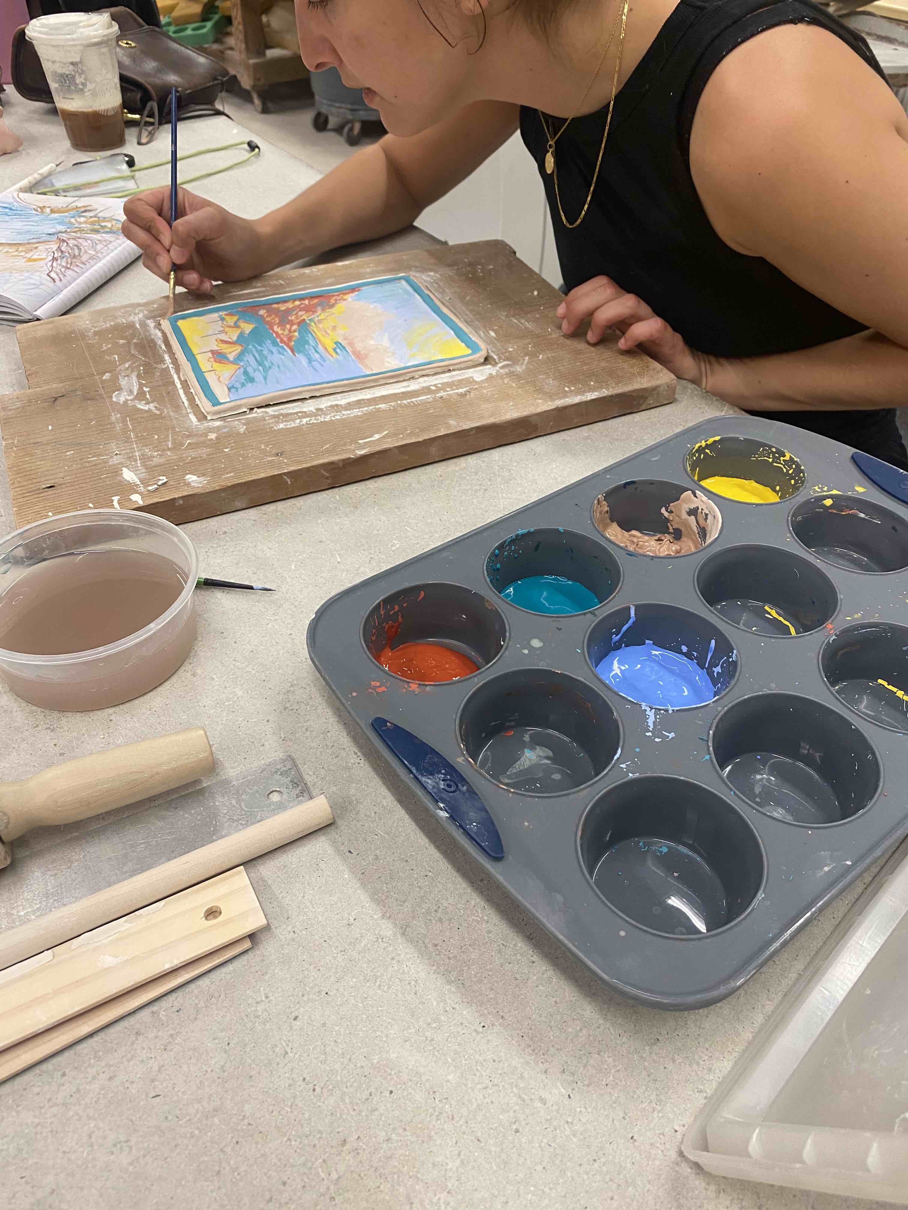 This image depicts a person painting on a ceramic tile.