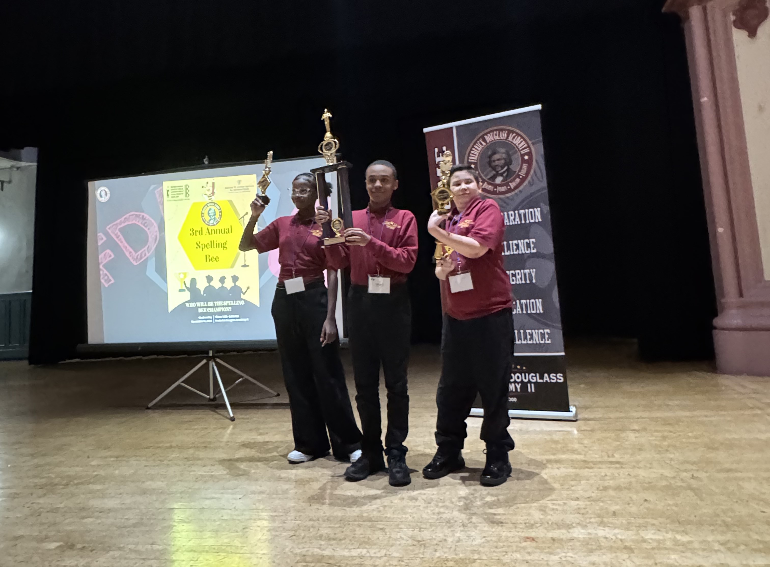 Three students standing in front of projector at spelling bee