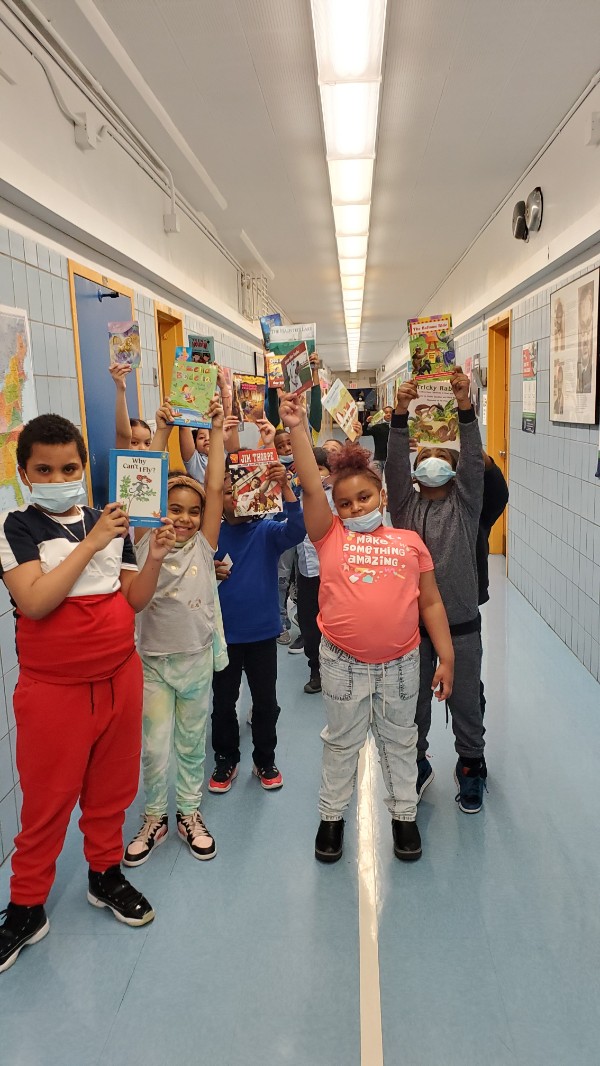 Kids showing off their books in the hallway of a school