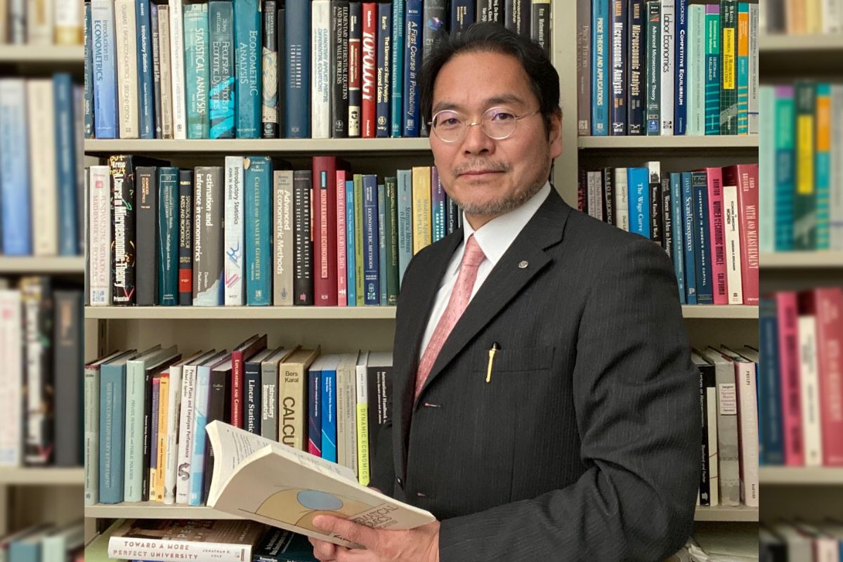 Satoshi standing in front of bookcase.