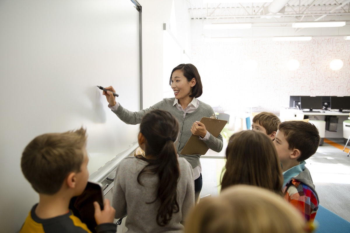 East asian woman teacher writing on a white board for a group of young students