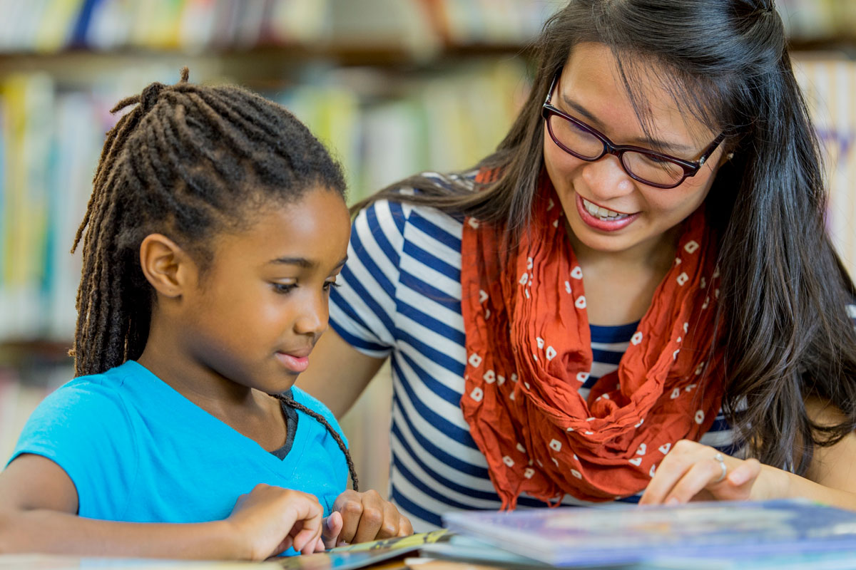 a teacher sitting with a student reading a book