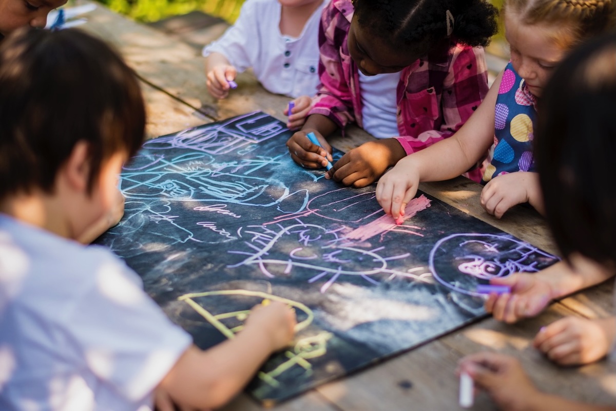 Children sitting on the ground and drawing with chalk