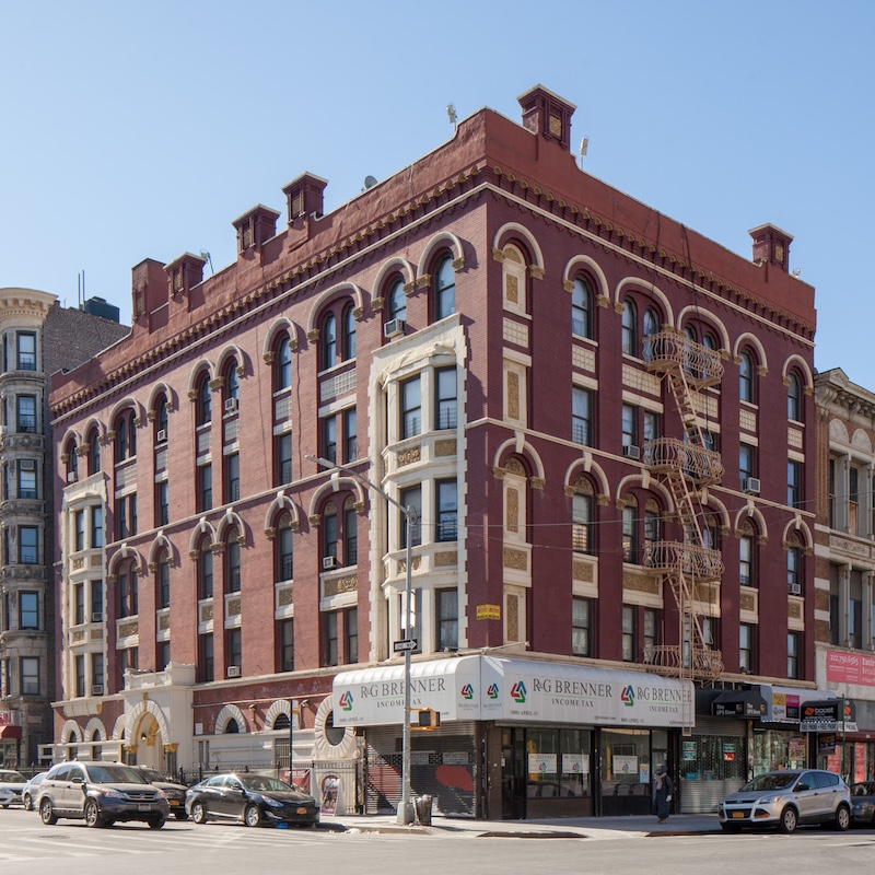 A five-sotry red brick building on a corner in Harlem