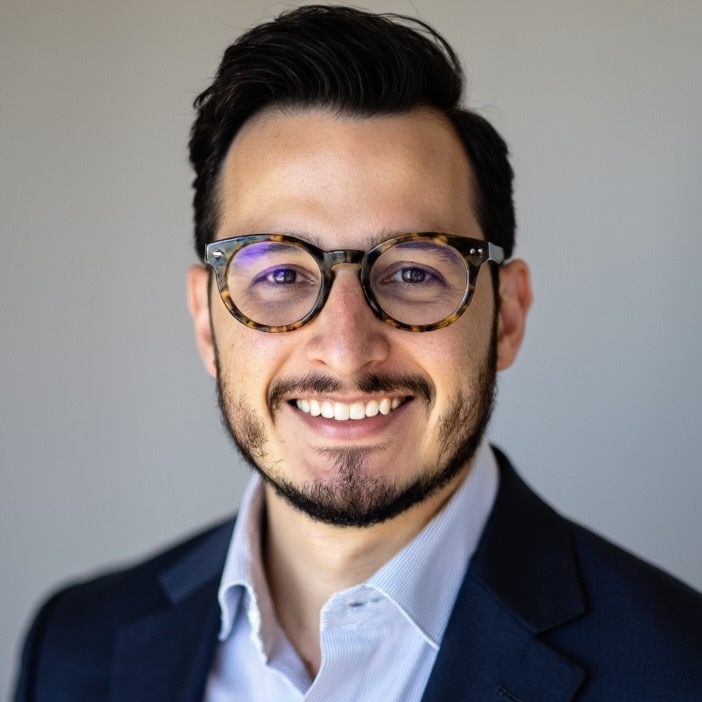 Adrian Rodriguez, a man with a bear and glasses, is smiling