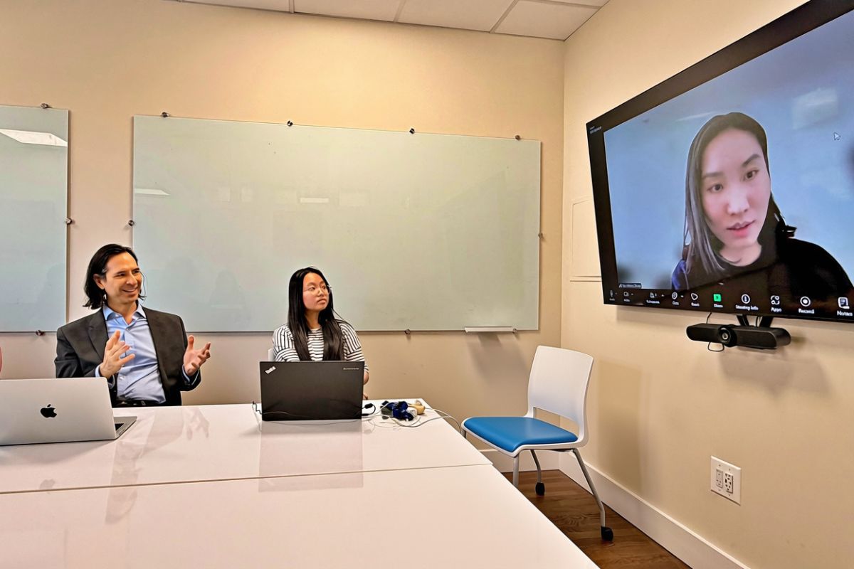 two people sitting at a table and looking at a third person on a television screen