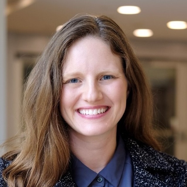 Alexandra Cooperstock, a woman with light brown hair, is smiling in a hallway