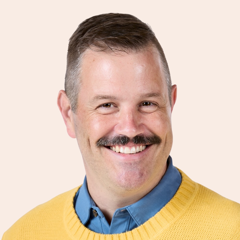 Matthew Henley, a man with a mustche and a yellow cardigan, smiles