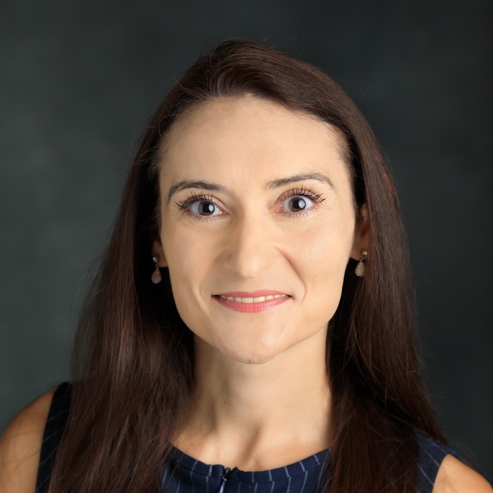 Zoi Traga Philippakos, a woman with long brown hair, smiles at the camera