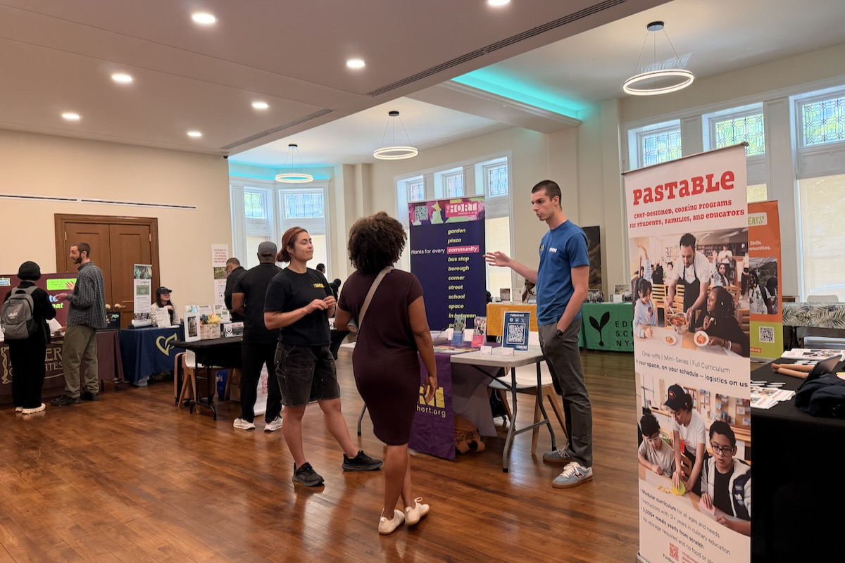 a group of people chatting in a room with several vendors at tables