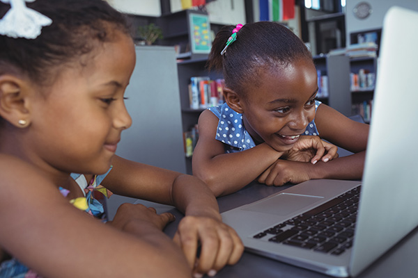 two school children working on a laptop in a classroom