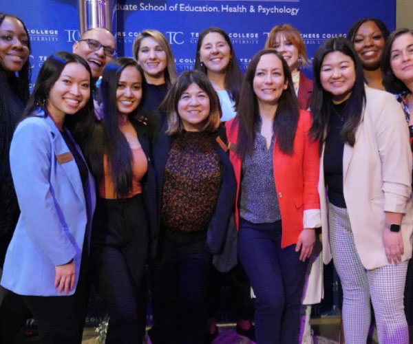 group of 12 people standing in two rows smiling in front of a blue background